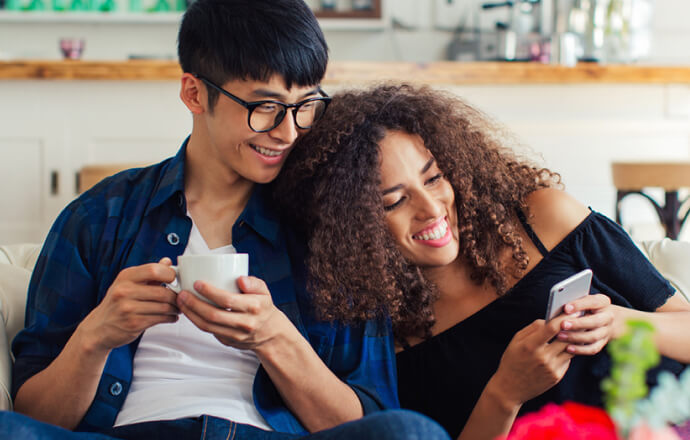 Un uomo e una donna sul divano che guardano il cellulare protetto da Norton 360 for Mobile.