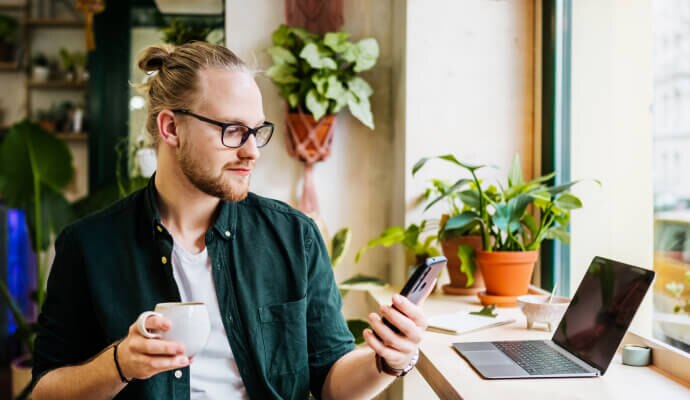 Uomo che beve una tazza di caffè mentre usa il cellulare protetto con Norton 360 for Mobile.