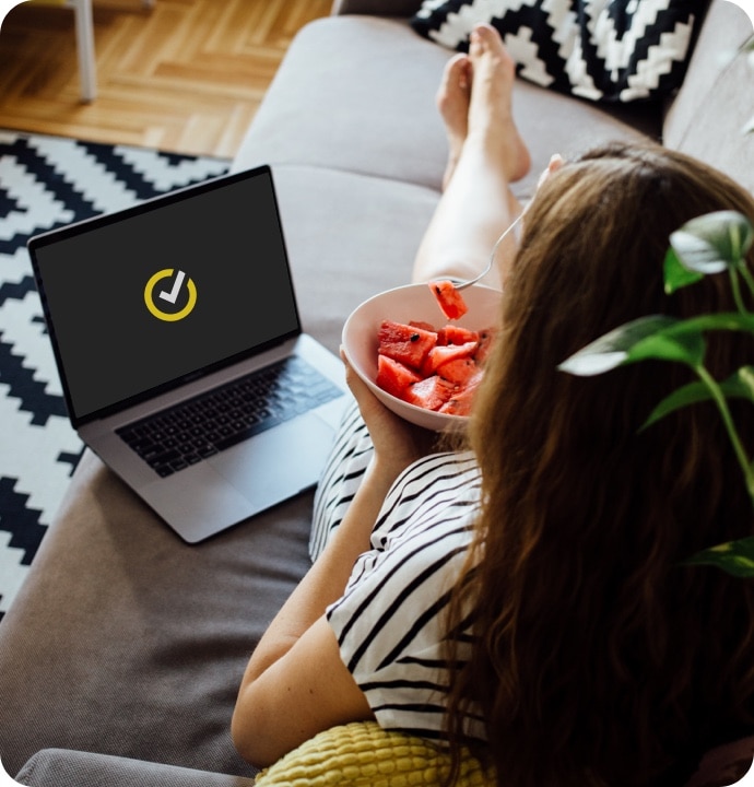 Donna che mangia un’anguria sul divano mentre usa un computer portatile su cui viene avviato Norton 360 AntiVirus Plus